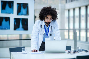 Front view portrait of serious male doctor standing in hospital, using laptop. - HPIF16136