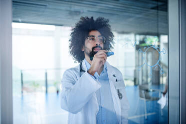 Porträt eines Arztes, der im Krankenhaus Notizen macht, Konzept des Corona-Virus, Aufnahme durch Glas. - HPIF16156