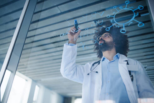 Portrait of doctor making notes in hospital, corona virus concept. Shot through glass. - HPIF16158