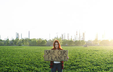 Porträt einer jungen Aktivistin mit Plakat, die im Freien vor einer Ölraffinerie steht und protestiert. - HPIF16181