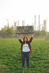 Porträt einer jungen Aktivistin mit Plakat, die im Freien vor einer Ölraffinerie steht und protestiert. - HPIF16182
