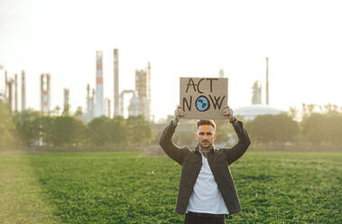 Porträt eines jungen Aktivisten mit Plakat, der im Freien vor einer Ölraffinerie steht und protestiert. - HPIF16184