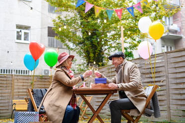 Porträt eines glücklichen älteren Paares mit Wein in einem Straßencafé in der Stadt, das seinen Geburtstag feiert. - HPIF16206
