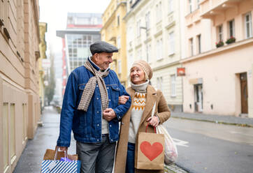 Porträt eines glücklichen älteren Paares, das auf einer Straße in der Stadt spazieren geht und Einkaufstüten trägt. - HPIF16215