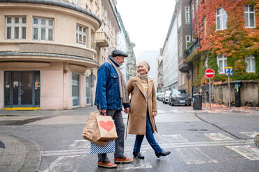 Porträt eines glücklichen älteren Paares, das auf einer Straße in der Stadt spazieren geht und Einkaufstüten trägt. - HPIF16218