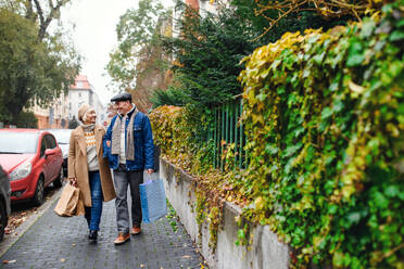 Porträt eines glücklichen älteren Paares, das auf einer Straße in der Stadt spazieren geht und Einkaufstüten trägt. - HPIF16219