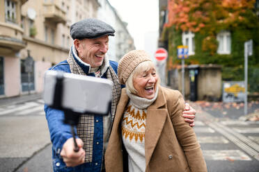 Portrait of happy senior couple walking outdoors on street in city, taking selfie. - HPIF16222