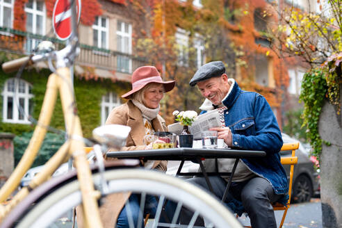 Glückliche ältere Menschen sitzen in einem Café im Freien in der Stadt und lesen Zeitungen. - HPIF16224