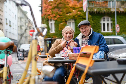 Glückliche ältere Menschen sitzen in einem Café im Freien in der Stadt und schauen in die Kamera. - HPIF16227