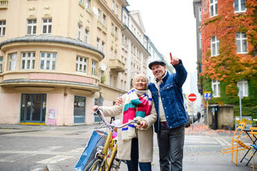 Porträt eines glücklichen älteren Paares mit Fahrrad im Freien auf einer Straße in der Stadt. - HPIF16234