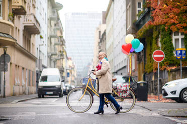 Porträt einer älteren Frau mit Fahrrad beim Überqueren der Straße im Freien in der Stadt. - HPIF16238