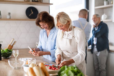 Front view of group of cheerful senior friends at dinner party at home, cooking. - HPIF16255