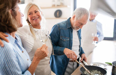 Frontansicht einer Gruppe fröhlicher älterer Freunde bei einer Dinnerparty zu Hause, beim Kochen. - HPIF16262