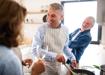 Front view of group of cheerful senior friends at dinner party at home, cooking. - HPIF16264