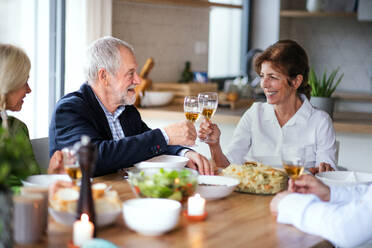 Eine Gruppe älterer Freunde genießt eine Dinnerparty zu Hause und stößt mit Gläsern an. - HPIF16272