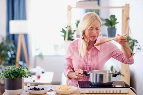 Vorderansicht einer älteren Frau, die in der Küche kocht und Nudeln im Topf umrührt. - HPIF16308