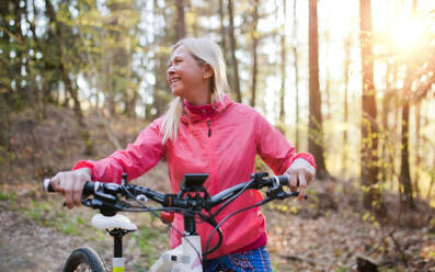 Active senior woman with e-bike cycling outdoors in nature. Copy space. - HPIF16350