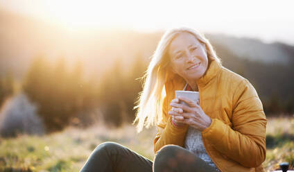 Attraktive ältere Frau sitzt im Freien in der Natur bei Sonnenuntergang, entspannt mit Kaffee. Kopieren Raum. - HPIF16361