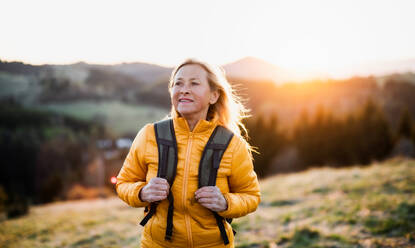 Attraktive ältere Frau mit Rucksack zu Fuß im Freien in der Natur bei Sonnenuntergang, Wandern. - HPIF16368