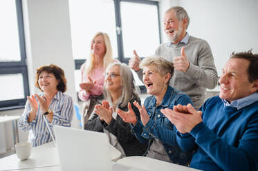 Eine Gruppe fröhlicher Senioren, die lachend und klatschend am Computer- und Technologieunterricht teilnehmen. - HPIF16415