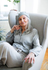 Studio-Porträt einer älteren Frau mit grauer Baskenmütze, die in einem Haus vor einem dunklen Hintergrund sitzt. - HPIF16418