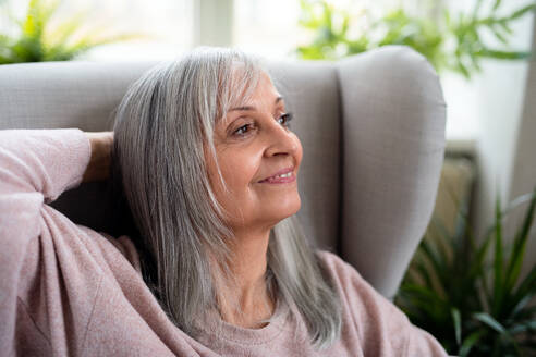 Porträt einer glücklichen älteren Frau, die zu Hause sitzt, in der Vorderansicht. - HPIF16430