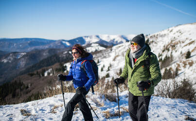 Älteres Paar mit Nordic-Walking-Stöcken beim Wandern in der verschneiten Winternatur, Konzept des gesunden Lebensstils. - HPIF16455