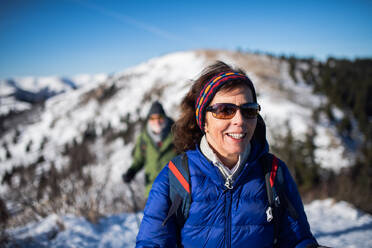 Porträt einer älteren Frau mit Ehemann beim Wandern in verschneiter Winterlandschaft. - HPIF16459