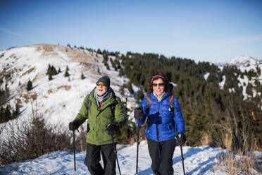 Älteres Paar mit Nordic-Walking-Stöcken beim Wandern in der verschneiten Winternatur, Konzept des gesunden Lebensstils. - HPIF16460