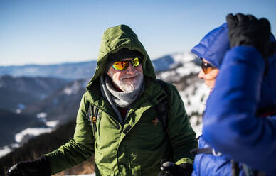 Älteres Wanderpaar, das sich in der verschneiten Winterlandschaft ausruht und sich unterhält. - HPIF16461