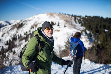 Älteres Paar mit Nordic-Walking-Stöcken beim Wandern in der verschneiten Winternatur, Konzept des gesunden Lebensstils. - HPIF16462