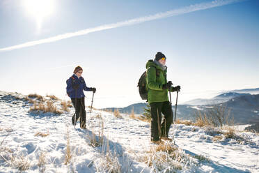 Älteres Paar mit Nordic-Walking-Stöcken beim Wandern in der verschneiten Winternatur, Konzept des gesunden Lebensstils. - HPIF16464