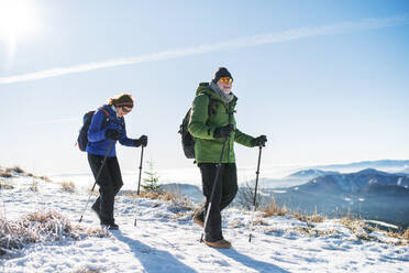 Älteres Paar mit Nordic-Walking-Stöcken beim Wandern in der verschneiten Winternatur, Konzept des gesunden Lebensstils. - HPIF16465