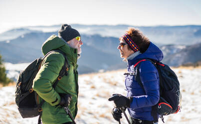 Älteres Wanderpaar, das sich in der verschneiten Winterlandschaft ausruht und sich unterhält. - HPIF16470