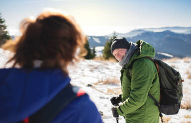 Älteres Wandererpaar mit Nordic-Walking-Stöcken in verschneiter Winternatur, rastend. - HPIF16473