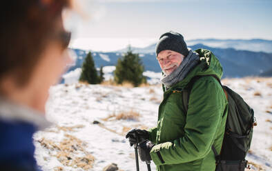 Älteres Wandererpaar mit Nordic-Walking-Stöcken in verschneiter Winternatur, rastend. - HPIF16474