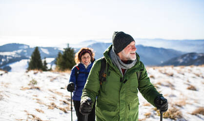 Senior couple with nordic walking poles hiking in snow-covered winter nature, healthy lifestyle concept. - HPIF16476