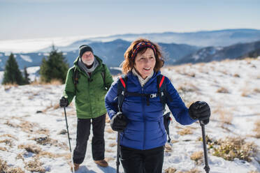 Senior couple with nordic walking poles hiking in snow-covered winter nature, healthy lifestyle concept. - HPIF16479