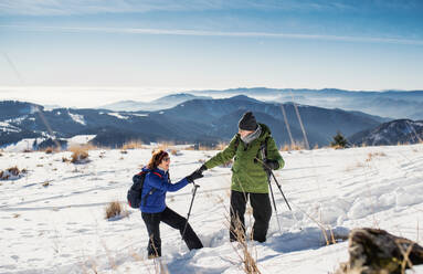 Älteres Paar mit Nordic-Walking-Stöcken beim Wandern in der verschneiten Winternatur, Konzept des gesunden Lebensstils. - HPIF16486