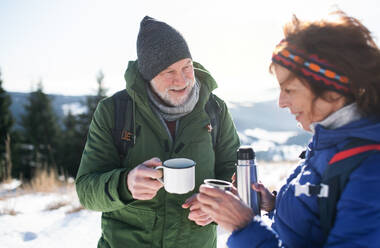 Senior couple hikers resting in snow-covered winter nature, drinking hot tea. - HPIF16491