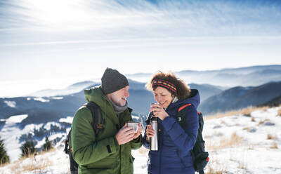 Senior couple hikers resting in snow-covered winter nature, drinking hot tea. - HPIF16492