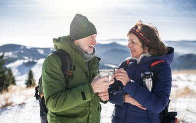 Senior couple hikers resting in snow-covered winter nature, drinking hot tea. - HPIF16493