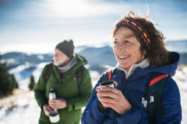 Senior couple hikers resting in snow-covered winter nature, drinking hot tea. - HPIF16494