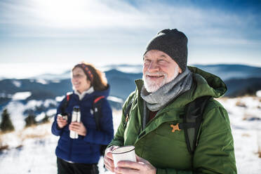 Älteres Wanderpaar ruht sich in der verschneiten Winternatur aus und trinkt heißen Tee. - HPIF16495