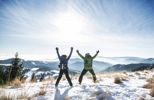 Rear view of cheerful senior couple hikers in snow-covered winter nature, jumping. - HPIF16502