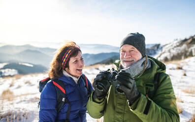 Porträt eines älteren Wanderpaares mit Fernglas in verschneiter Winterlandschaft. - HPIF16505