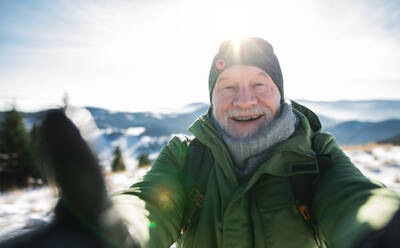 Front view portrait of senior man standing in snow-covered winter nature, looking at camera. - HPIF16506