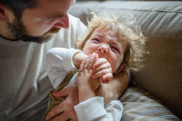 Reifer Vater mit kleiner, kranker, weinender Kleinkind-Tochter drinnen zu Hause. - HPIF16525