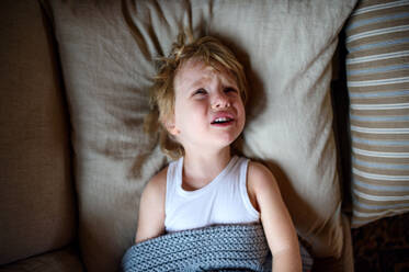 Draufsicht auf einen weinenden kleinen kranken Jungen, der zu Hause im Bett liegt. - HPIF16526