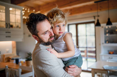 Father with small sick unhappy son indoors at home, holding and comforting him. - HPIF16529